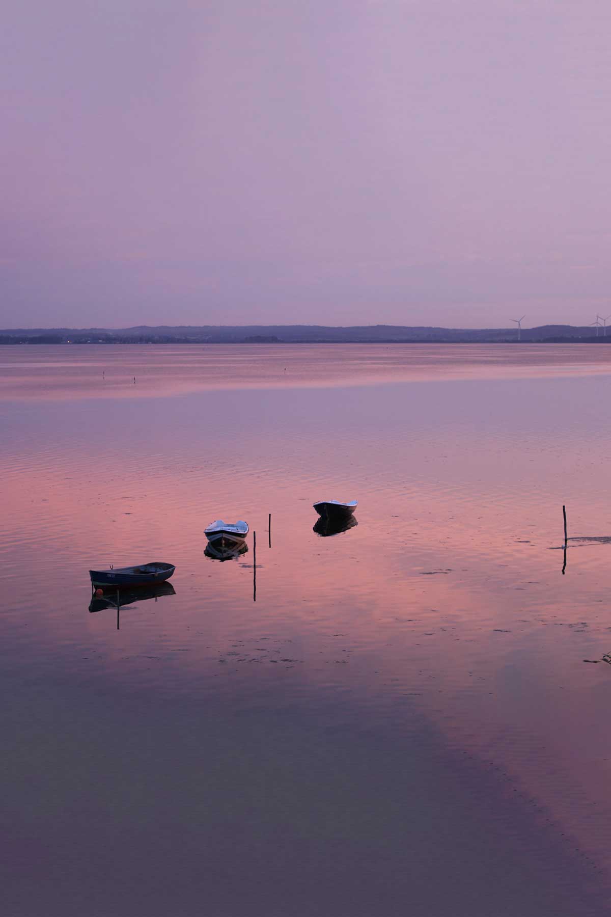 Trzy puste łodzie pływające po jeziorze w trakcie zachodu słońca.